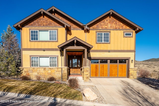 craftsman-style house with stone siding, driveway, board and batten siding, and an attached garage