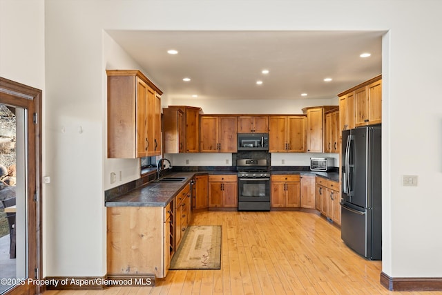 kitchen featuring a sink, stainless steel microwave, range with gas stovetop, black fridge with ice dispenser, and light wood finished floors