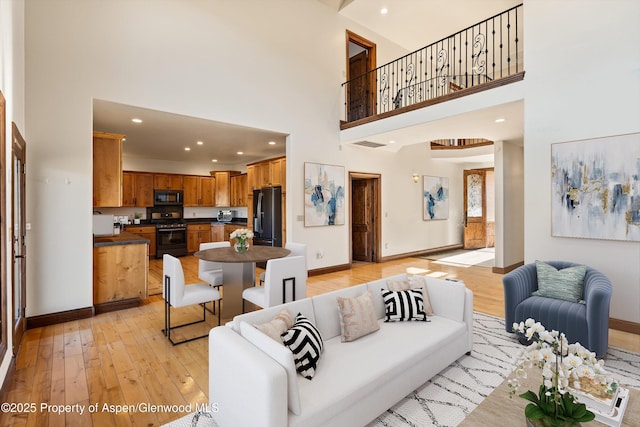 living room featuring a towering ceiling, baseboards, and light wood finished floors