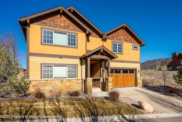 craftsman-style house with an attached garage, board and batten siding, driveway, stone siding, and a mountain view