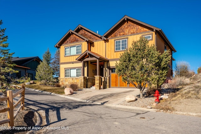 craftsman-style house featuring stone siding, board and batten siding, concrete driveway, and fence