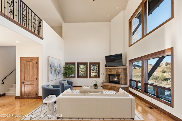 living area featuring baseboards, stairs, light wood-type flooring, a fireplace, and a high ceiling