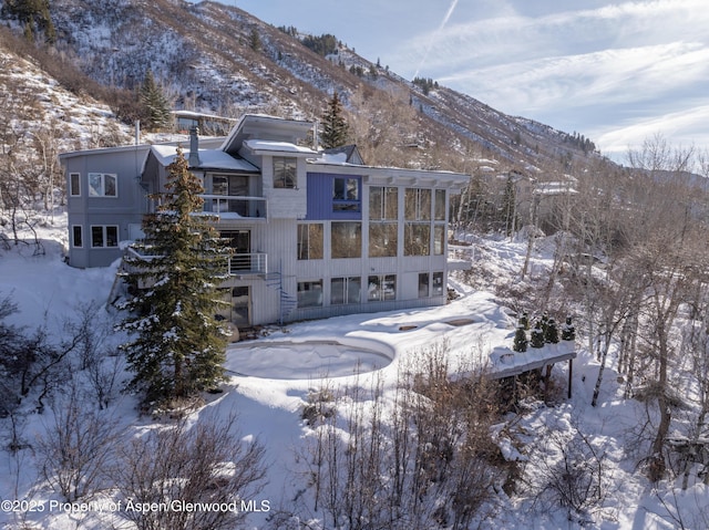 snow covered rear of property with a mountain view and a sunroom