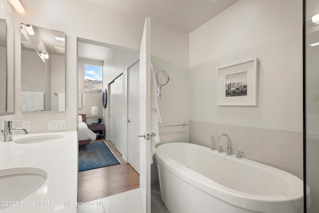 ensuite bathroom with double vanity, a soaking tub, wood finished floors, and a sink