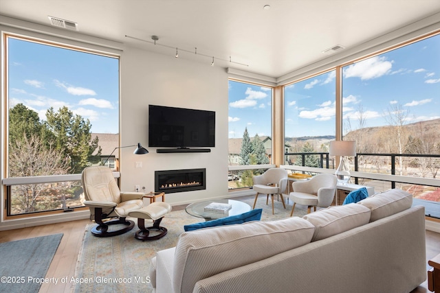 living room featuring visible vents, a wall of windows, a glass covered fireplace, and wood finished floors