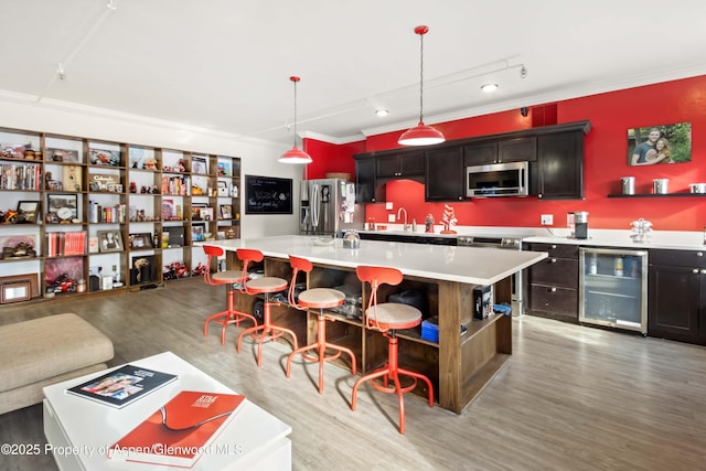 kitchen with stainless steel appliances, decorative light fixtures, an island with sink, rail lighting, and wine cooler