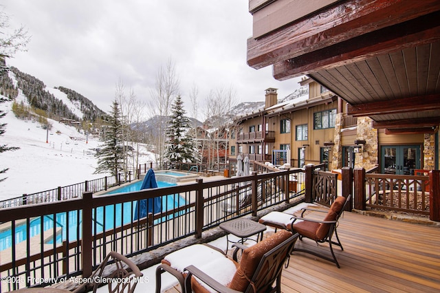 snow covered deck with french doors, a mountain view, and a community pool