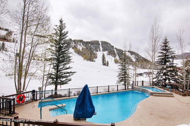 snow covered pool featuring a pool with connected hot tub, a patio, and a mountain view