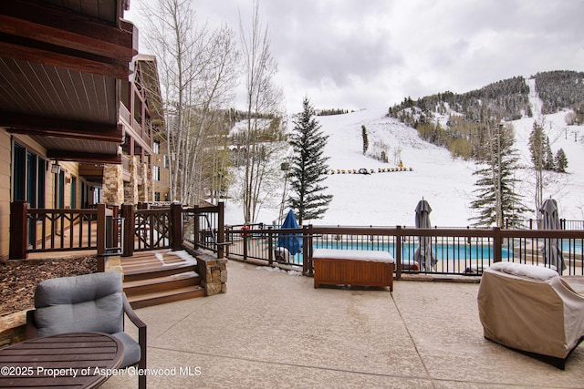 snow covered patio with a grill, a mountain view, and a fenced in pool