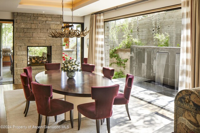 dining area with a tray ceiling, an inviting chandelier, and a stone fireplace