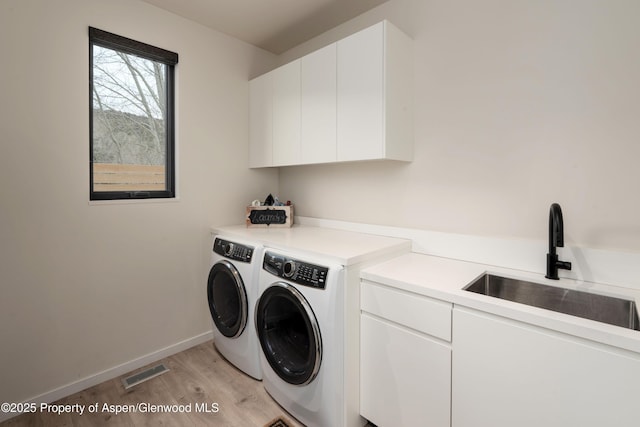 washroom with washing machine and clothes dryer, visible vents, light wood-style flooring, cabinet space, and a sink