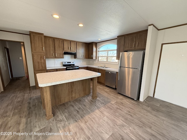 kitchen featuring stainless steel appliances, sink, a center island, a textured ceiling, and light hardwood / wood-style flooring