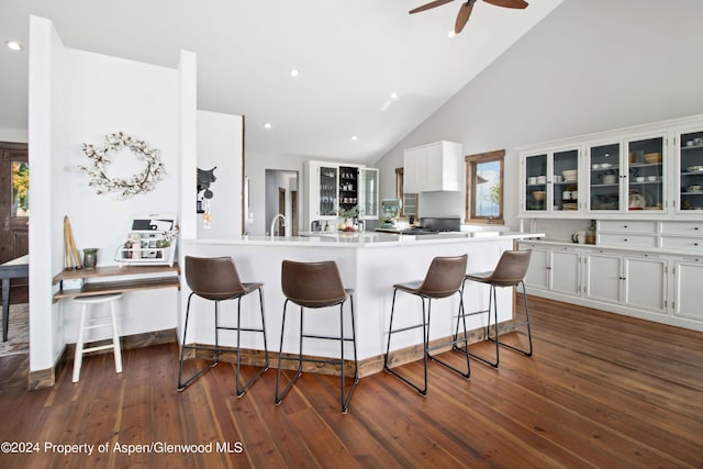 kitchen featuring kitchen peninsula, a breakfast bar, white cabinets, and high vaulted ceiling