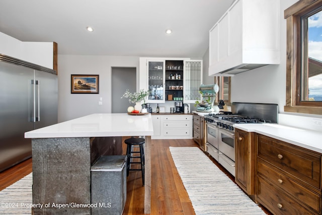 kitchen with a kitchen breakfast bar, dark hardwood / wood-style flooring, custom exhaust hood, high end appliances, and white cabinetry