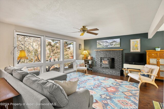 living room with a wood stove, ceiling fan, dark hardwood / wood-style flooring, and a textured ceiling