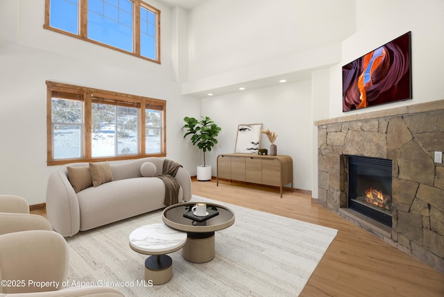 living room with a fireplace, a towering ceiling, baseboards, and wood finished floors