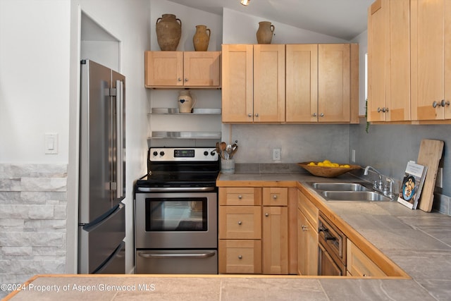 kitchen featuring appliances with stainless steel finishes, a sink, light brown cabinets, tile countertops, and vaulted ceiling