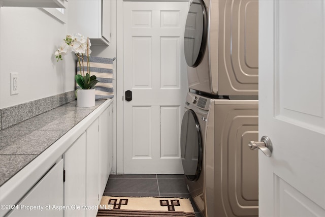washroom featuring dark tile patterned flooring, stacked washer and dryer, and cabinet space