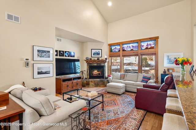 living room with high vaulted ceiling, a tile fireplace, wood finished floors, and visible vents