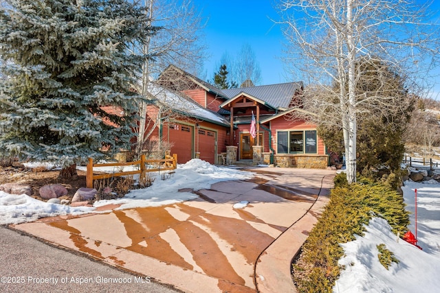 view of front of home with a garage, stone siding, metal roof, and driveway