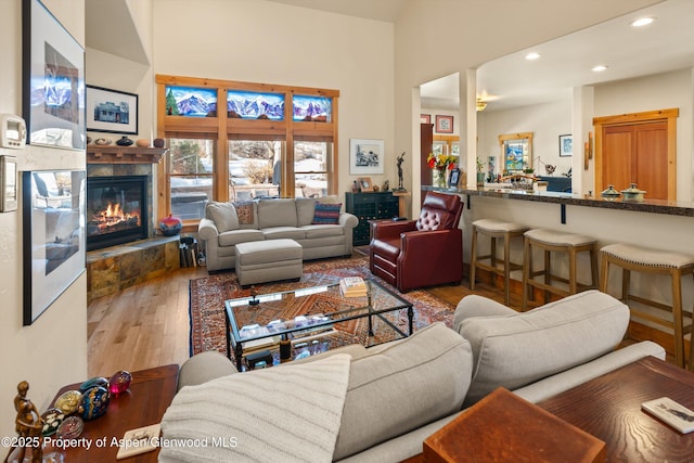 living area with wood finished floors, a glass covered fireplace, a high ceiling, and recessed lighting