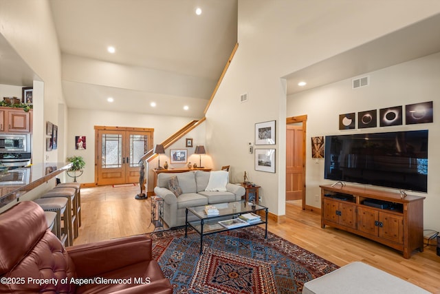 living room with high vaulted ceiling, french doors, visible vents, and light wood finished floors