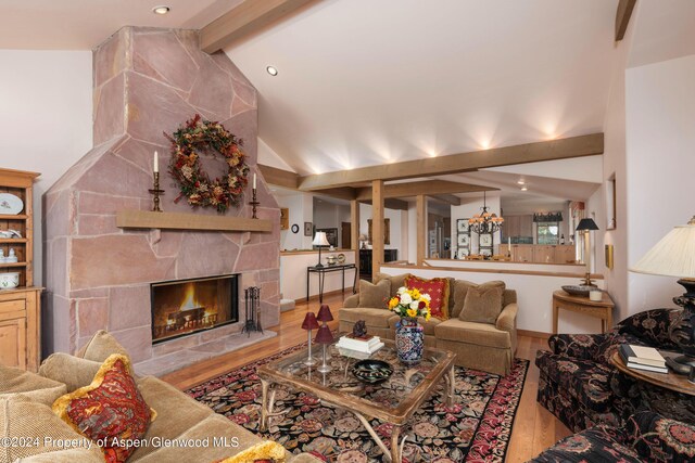 living room with lofted ceiling with beams, a stone fireplace, and light hardwood / wood-style flooring