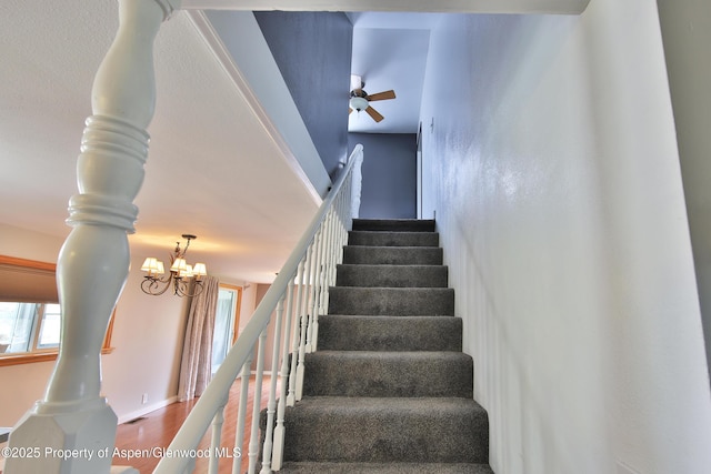 staircase featuring baseboards, a healthy amount of sunlight, wood finished floors, and ceiling fan with notable chandelier