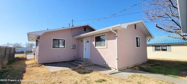 view of front facade with entry steps, fence, and stucco siding