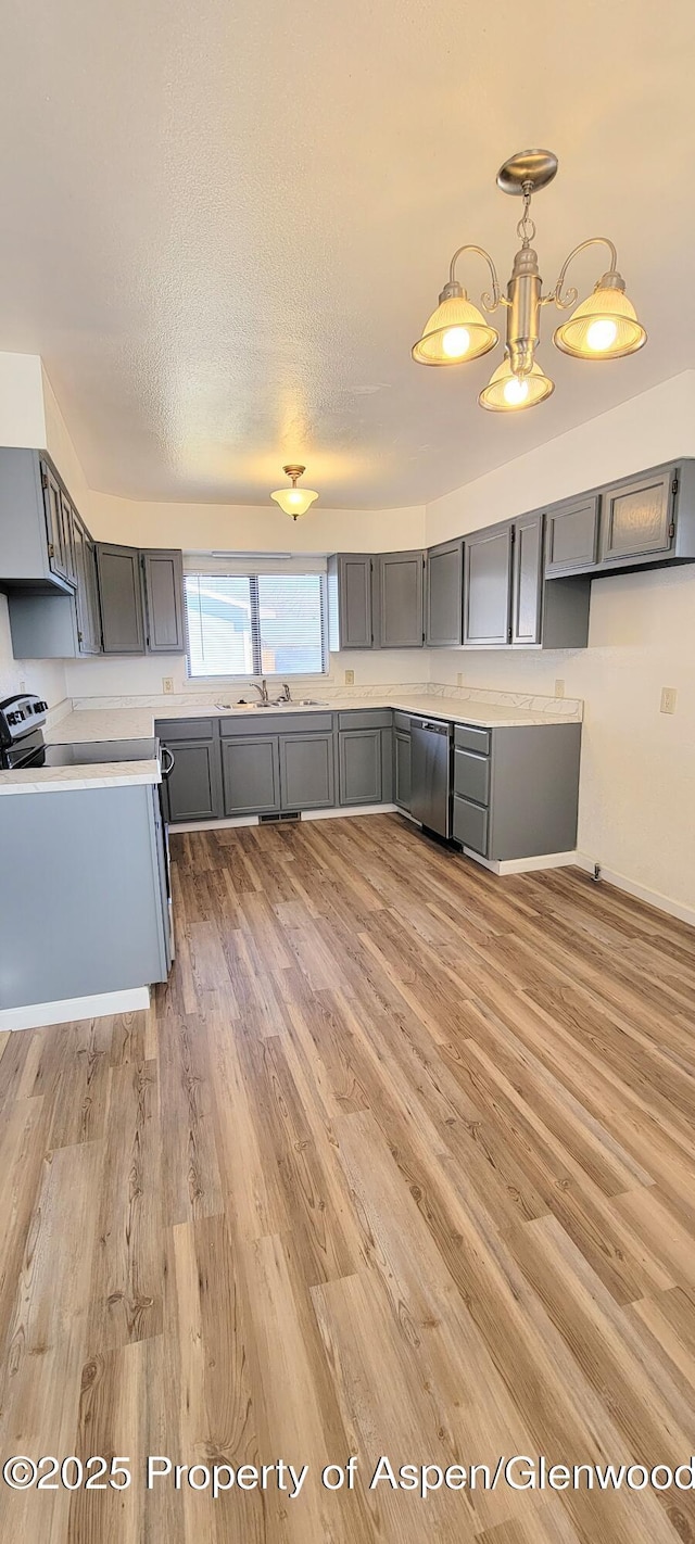 kitchen featuring gray cabinetry, pendant lighting, light wood-style floors, a textured ceiling, and stainless steel dishwasher