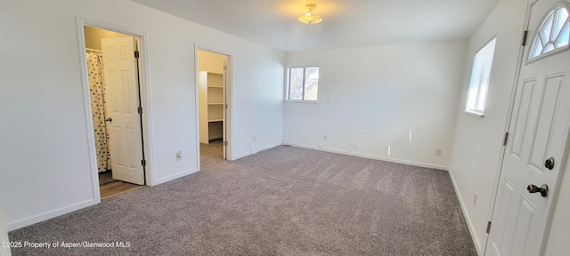 unfurnished bedroom with a walk in closet, multiple windows, baseboards, and carpet flooring