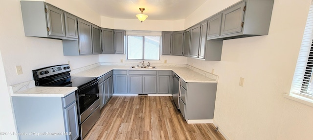 kitchen with light wood-style flooring, gray cabinets, a sink, stainless steel appliances, and light countertops