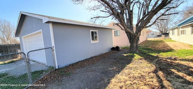 view of home's exterior with a gate, a detached garage, an outdoor structure, and fence