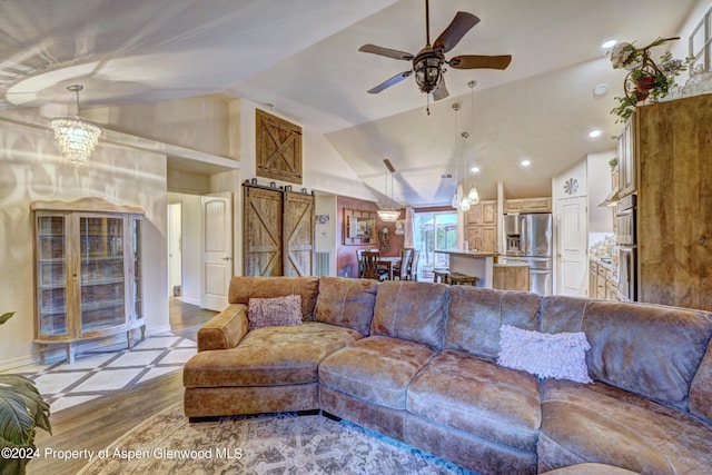 living room with ceiling fan with notable chandelier, a barn door, and vaulted ceiling