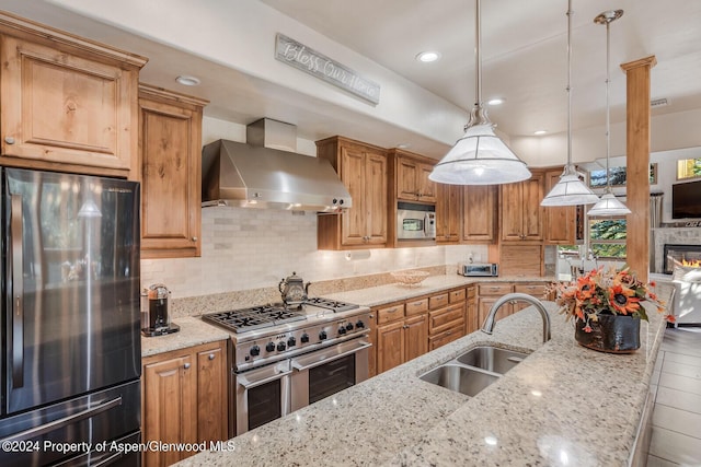 kitchen featuring light stone countertops, stainless steel appliances, hanging light fixtures, and wall chimney exhaust hood