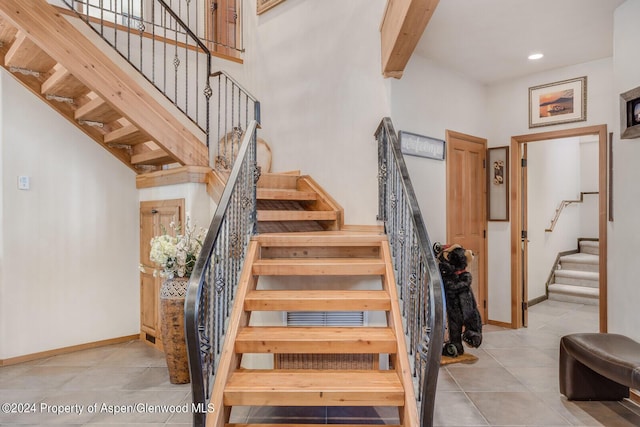 stairway with beam ceiling, a towering ceiling, and tile patterned floors