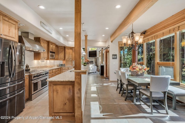 kitchen with beam ceiling, light stone countertops, wall chimney exhaust hood, a notable chandelier, and appliances with stainless steel finishes