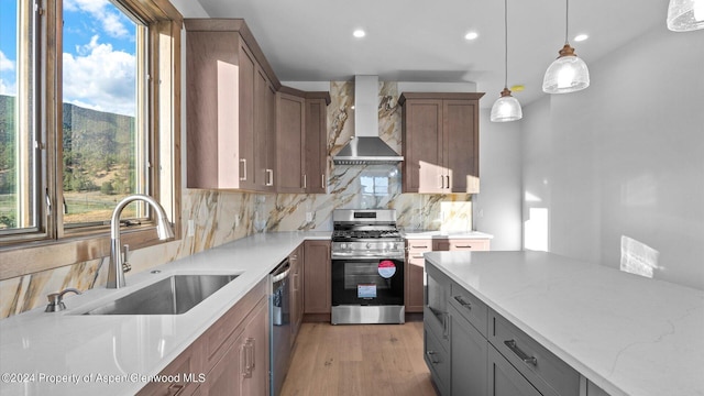 kitchen with wall chimney range hood, sink, a wealth of natural light, appliances with stainless steel finishes, and decorative light fixtures