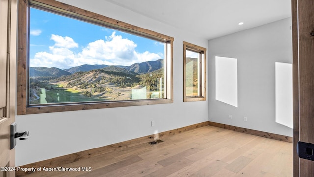 unfurnished bedroom with a mountain view, light hardwood / wood-style flooring, and multiple windows