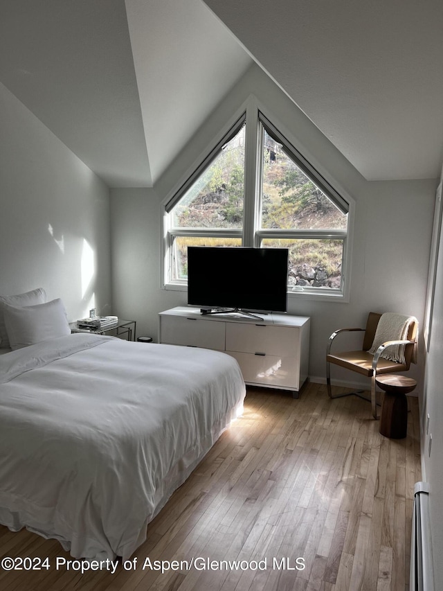 bedroom featuring lofted ceiling, light hardwood / wood-style flooring, and a baseboard heating unit