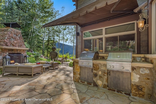 view of patio featuring a mountain view, an outdoor living space with a fireplace, grilling area, and exterior kitchen