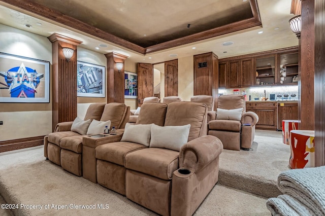 carpeted home theater room with a tray ceiling and decorative columns