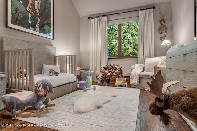 bedroom featuring a crib, wood-type flooring, and lofted ceiling