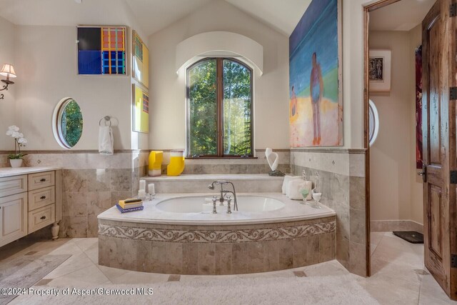 bathroom featuring a relaxing tiled tub, tile patterned floors, vaulted ceiling, vanity, and tile walls