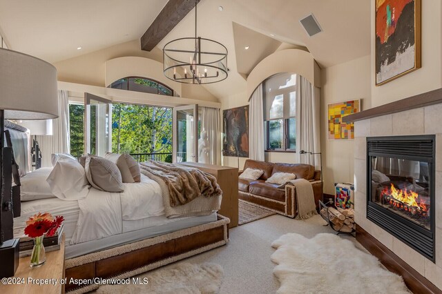 carpeted bedroom with a tile fireplace, lofted ceiling with beams, and an inviting chandelier