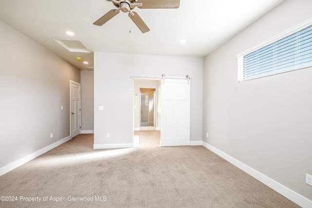 unfurnished bedroom featuring ceiling fan, a barn door, light colored carpet, and ensuite bath