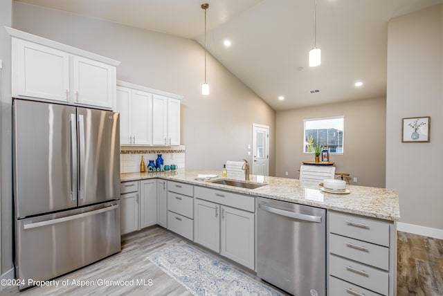 kitchen with sink, stainless steel appliances, backsplash, decorative light fixtures, and light wood-type flooring