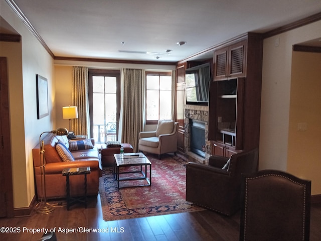 living area with crown molding, wood finished floors, baseboards, and a stone fireplace