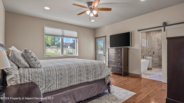 bedroom with ceiling fan, a barn door, ensuite bathroom, and light hardwood / wood-style flooring