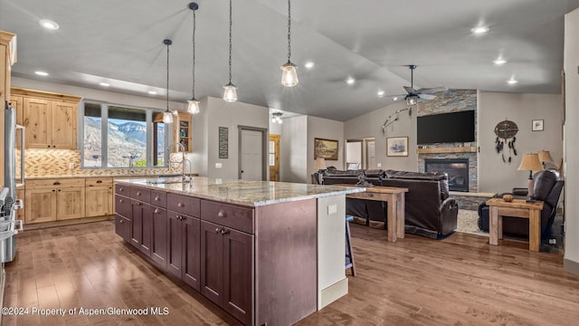 kitchen with sink, light stone counters, backsplash, lofted ceiling, and a fireplace